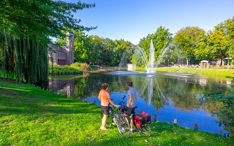 Ein wunderschönes Sommerfoto aus der Stadt Cottbus, auf dem zwei Radler einen Teich am Brandenburgischen Landesmuseum für moderne Kunst bewundern