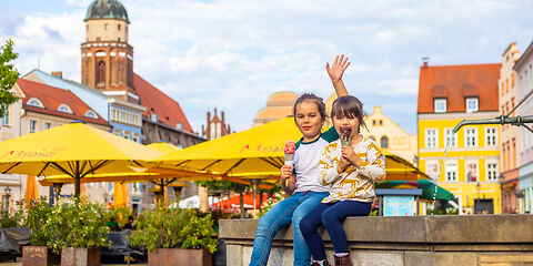 Auf dem Foto ist der Altmarkt der Stadt Cottbus zu sehen. Zwei kleine Mädchen sitzen auf dem historischen Brunnen und essen ein Eis. Im Hintergrund befindet sich der Turm von der Oberkirche.