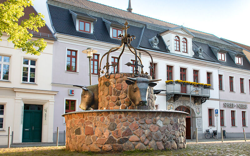 Der Bullwinkel am Kavalierhaus in Spremberg zeigt einen beeindruckenden Brunnen mit Bullköpfern, die das Wahrzeichen des Platzes bilden. Im Hintergrund erhebt sich das helle Kavalierhaus, das dem historischen Ensemble eine elegante Note verleiht.