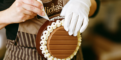 Auf dem Foto ist eine Torte zu sehen, die von einer Frau liebevoll verziert wird. Das Logo „Felicitas“ ist gut sichtbar auf ihrer Schürze. 