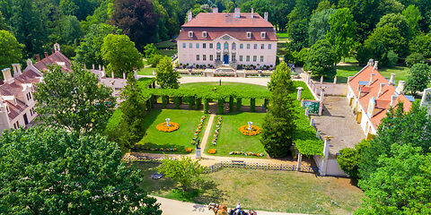 Auf dem Foto ist das Schloss und der Park von Fürst Pückler in Branitz zu sehen. Die weitläufigen grünen Flächen und die sommerliche Sonne laden zu einem Spaziergang ein.