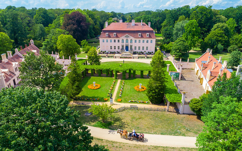 Auf dem Foto ist das Schloss und der Park von Fürst Pückler in Branitz zu sehen. Die weitläufigen grünen Flächen und die sommerliche Sonne laden zu einem Spaziergang ein.