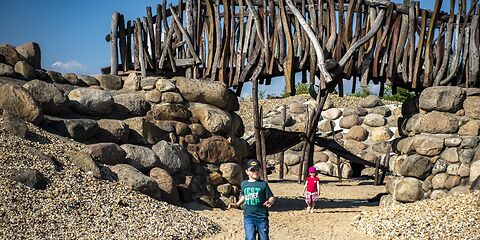 Auf dem Foto sind zwei Kinder auf einem Spielplatz mit einer Steinmauer und einer Holzbrücke zu sehen. 