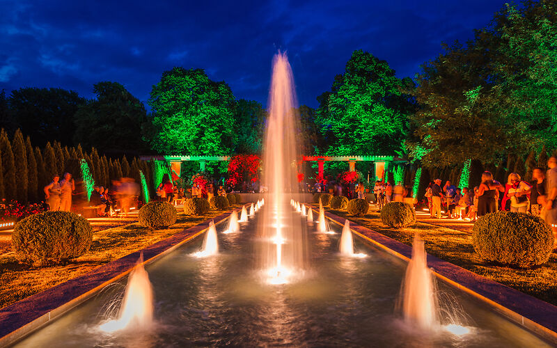 Die Großen Wasserspiele in der bunten Lichtillumination am Spätabend mit vielen Besuchern. 