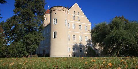 Eine Sommeraufnahme des Schlosses Spremberg zeigt die hellen, strahlenden Wände des Gebäudes, umgeben von üppigem Grün der Bäume. Das klare Wetter und das lebendige Grün verleihen der Szene eine frische, einladende Atmosphäre.