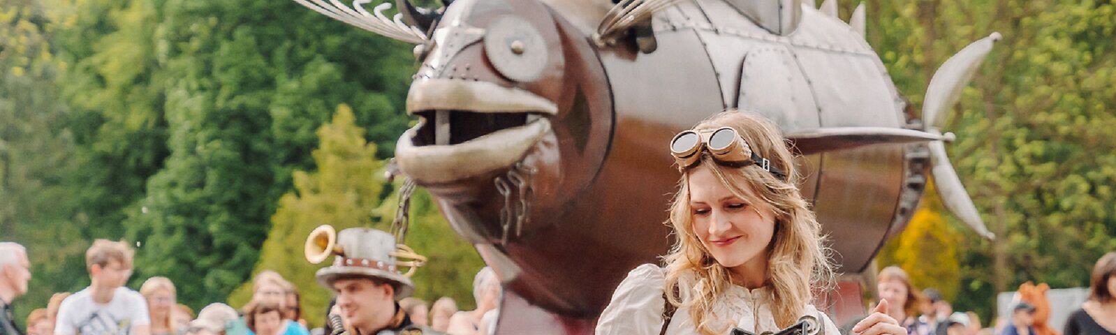 Auf dem Bild ist eine Steampunk-Fisch-Machine mit einer Frau mit einer futurischtischen Brille zu sehen. 